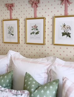 three framed pictures hang on the wall above a bed with white pillows and pink bows