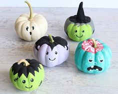 four painted pumpkins with faces on them sitting on a counter top next to each other