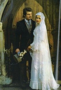 a bride and groom standing in front of an old wooden door, dressed in white