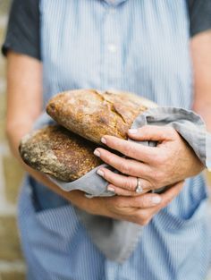 a man holding two loaves of bread in his hands and wearing a blue shirt