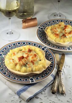 two blue and white plates topped with food next to glasses of wine on a table