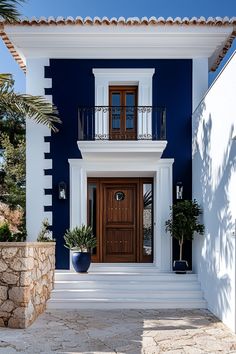 a blue and white house with two large plants on the front steps, and a brown door