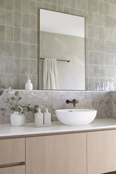 a bathroom sink sitting under a mirror next to a white vase and potted plant