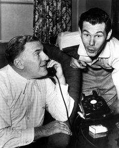 two men sitting on a couch talking on telephones and looking at each other's faces