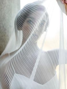 a woman wearing a white dress and veil with her hands on the window sill