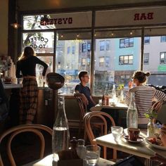 people sitting at tables in a restaurant with windows looking out onto the street and buildings