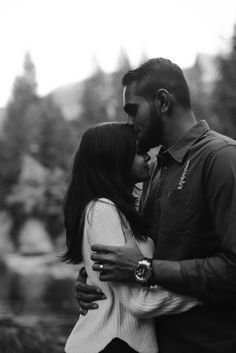 a man and woman kissing in front of trees