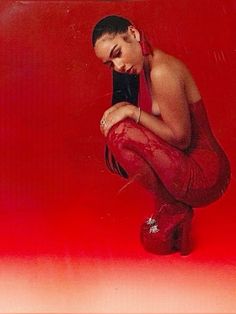 a woman sitting on top of a pair of red high heeled shoes in front of a red background