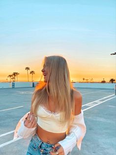 a woman with long blonde hair standing in an empty parking lot at sunset or sunrise