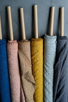 four different colored umbrellas are lined up in a row on a gray wall with wooden poles