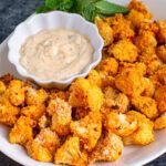 a white plate topped with tater tots next to a bowl of dip