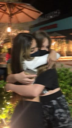 two young women hugging each other in front of an open umbrella outside at night time