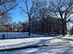 a person is walking through the snow in front of an old brick building and trees