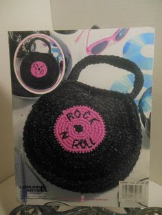 a crocheted black purse with pink logo on the front and side, sitting next to a pair of sunglasses