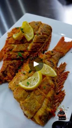 two pieces of fish on a white plate with lemon wedges and garnishes