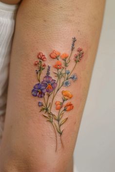 a woman's thigh with colorful flowers on the side and behind her is a tattoo