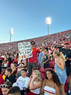 a group of people sitting in the stands at a football game with signs on their backs