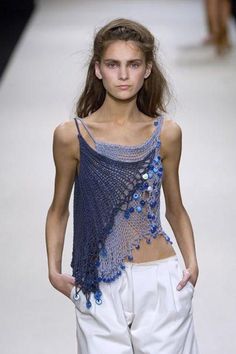 a model walks down the runway wearing white pants and a blue top with flowers on it