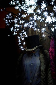 a mannequin wearing a top hat and fur coat in front of a tree with white lights