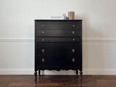 a black dresser sitting on top of a hard wood floor next to a white wall