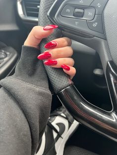 a woman's hand on the steering wheel of a car with red nail polish