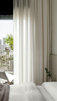 a white bed sitting next to a window covered in curtains