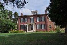 a large red brick house sitting in the middle of a lush green field next to trees