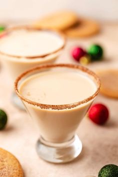 two glasses filled with white liquid next to cookies and candy canes on a table