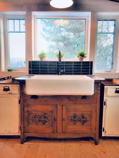 a kitchen sink sitting under a window in front of two windows with potted plants