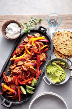 a platter filled with chicken, peppers and guacamole next to pita bread