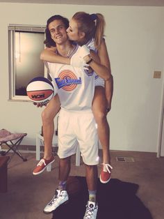 a man is holding a woman in his arms while she holds a basketball and smiles