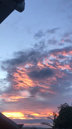 the sun is setting behind some clouds in the sky over a building and tree line