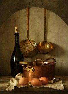 an old fashioned copper pot and some eggs on a table next to a wine bottle