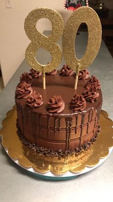 a birthday cake with chocolate frosting and gold numbers on top, sitting on a table