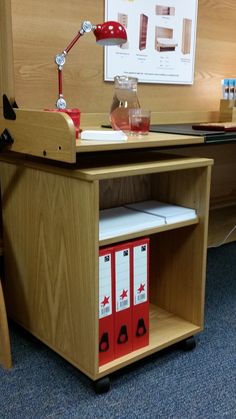 a wooden desk with red file folders and a lamp on top of it in an office