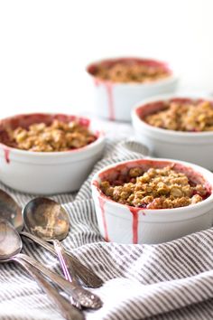 three bowls filled with food sitting on top of a table next to two spoons