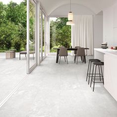 an open kitchen and dining room area with white walls, flooring and large windows