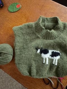 a green sweater with two black and white cows on it, next to yarn balls