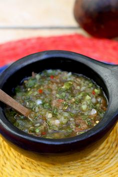 a black bowl filled with soup sitting on top of a yellow place mat next to a wooden spoon