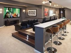 a large home theater with bar seating and two movie screens on the wall behind it