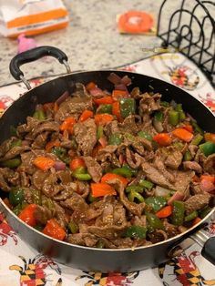 a pan filled with beef and peppers on top of a table next to utensils