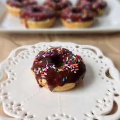 a chocolate covered doughnut sitting on top of a white doily with sprinkles