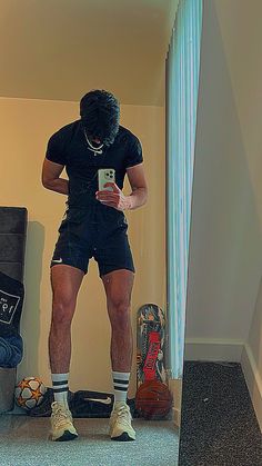 a man standing in front of a mirror looking at his cell phone while wearing shorts and socks