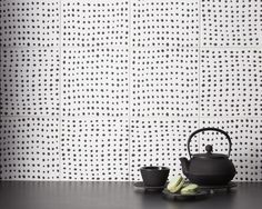 a tea pot and two cups sitting on a table in front of a wall with dots