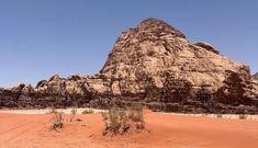 a large rock formation in the middle of a desert with sparse grass and bushes growing out of it