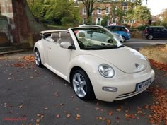 a white convertible car parked on the side of a road next to trees and leaves