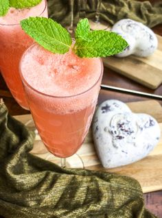 two glasses filled with watermelon and mint on top of a wooden cutting board