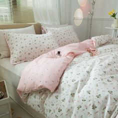 a bed covered in pink and white floral comforter next to a window with curtains