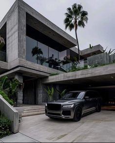 a black suv is parked in front of a large house with palm trees on the other side