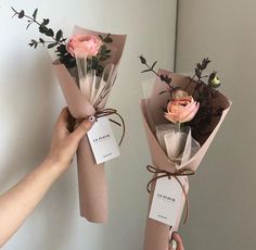 two flowers are wrapped in brown paper and tied with twine to each other, while being held by someone's hand